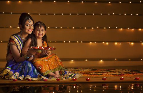 A young mother and daughter lighting diyas on Diwali