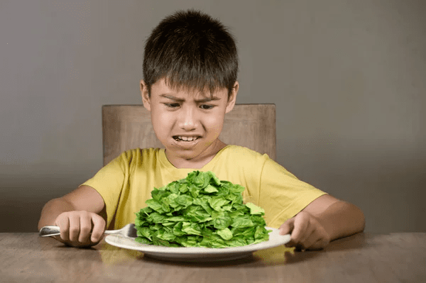 A young boy pushing away a plate of baby spinach