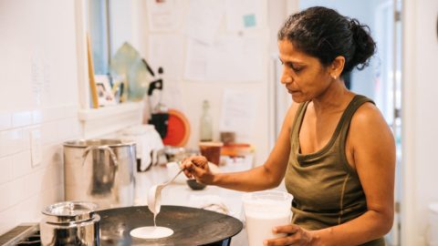 An Indian woman cooking dosa on iron dosa tawa